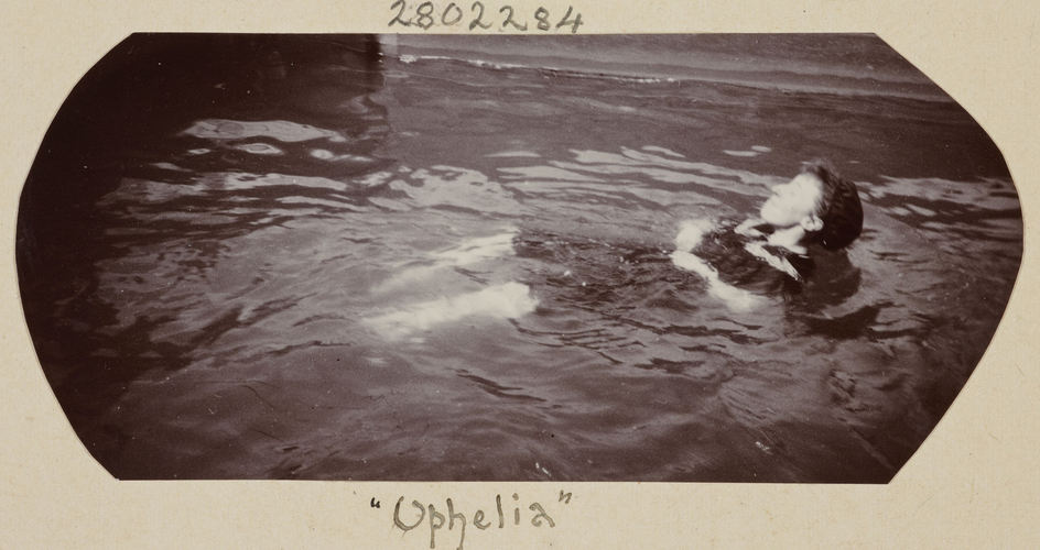 Sepia photograph of woman floating on her back in water. the woman's eyes are closed as she pretends to be drowned like Hamlet's Ophelia